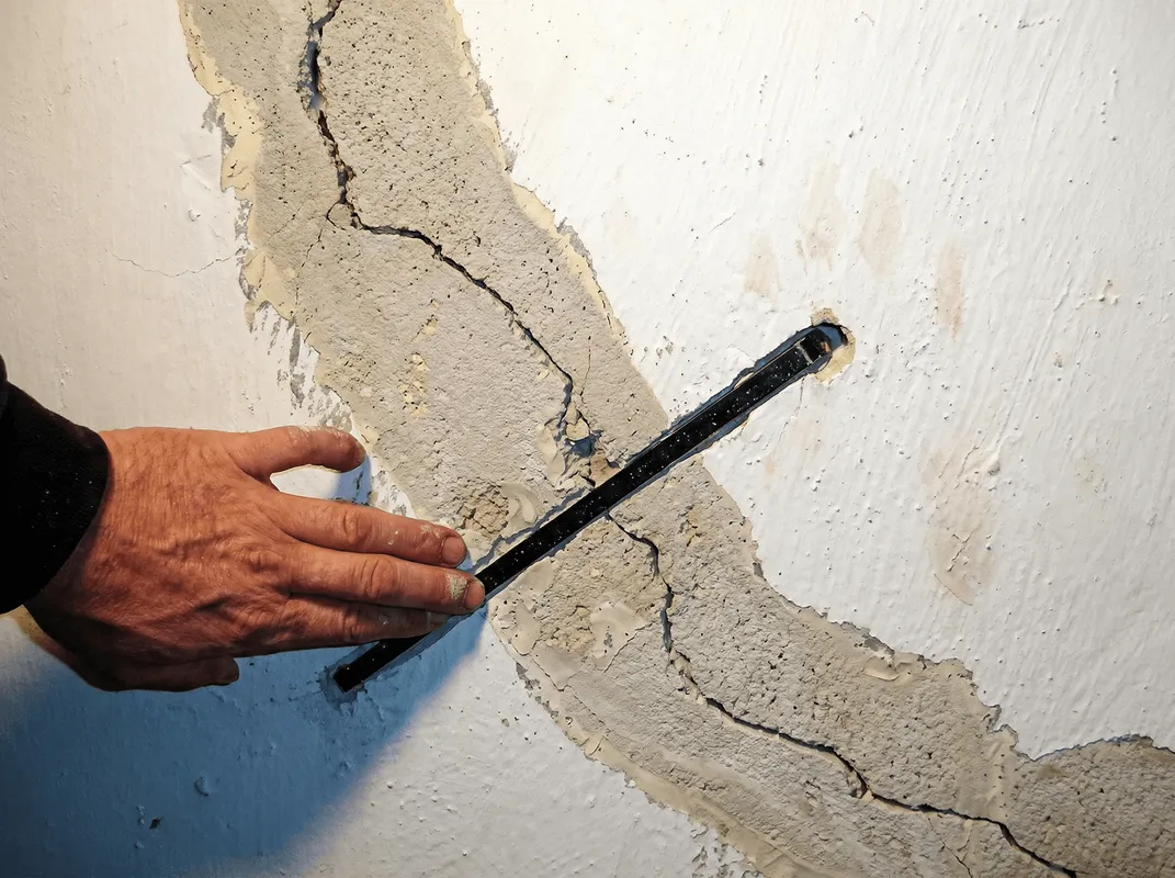A wall with a large crack is being inspected by a professional in Nashua, NH